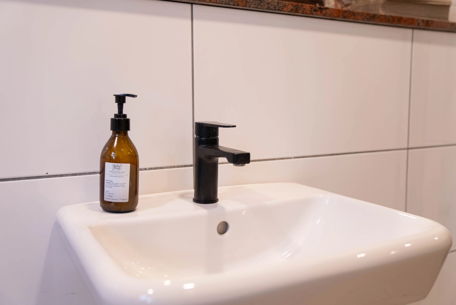 Alpakahof Dingen – Alpaka-Trekking – Dieses Bild zeigt ein modernes Badezimmer mit freigelegten Ziegelwänden, eleganten weißen Schränken und einem Waschtisch mit Granitplatte.