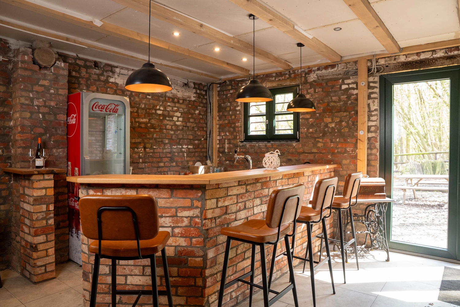 Alpakahof Dingen – Alpaka-Trekking – Das Bild zeigt eine ländliche Bauernhofszene mit Alpakas in einem hölzernen Unterstand und Gehege.