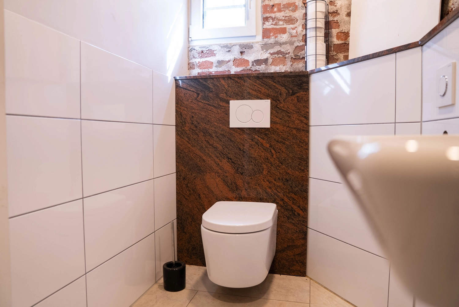 Alpakahof Dingen – Alpaka-Trekking – Dieses Bild zeigt ein modernes Badezimmer mit freigelegten Ziegelwänden, eleganten weißen Schränken und einem Waschtisch mit Granitplatte.