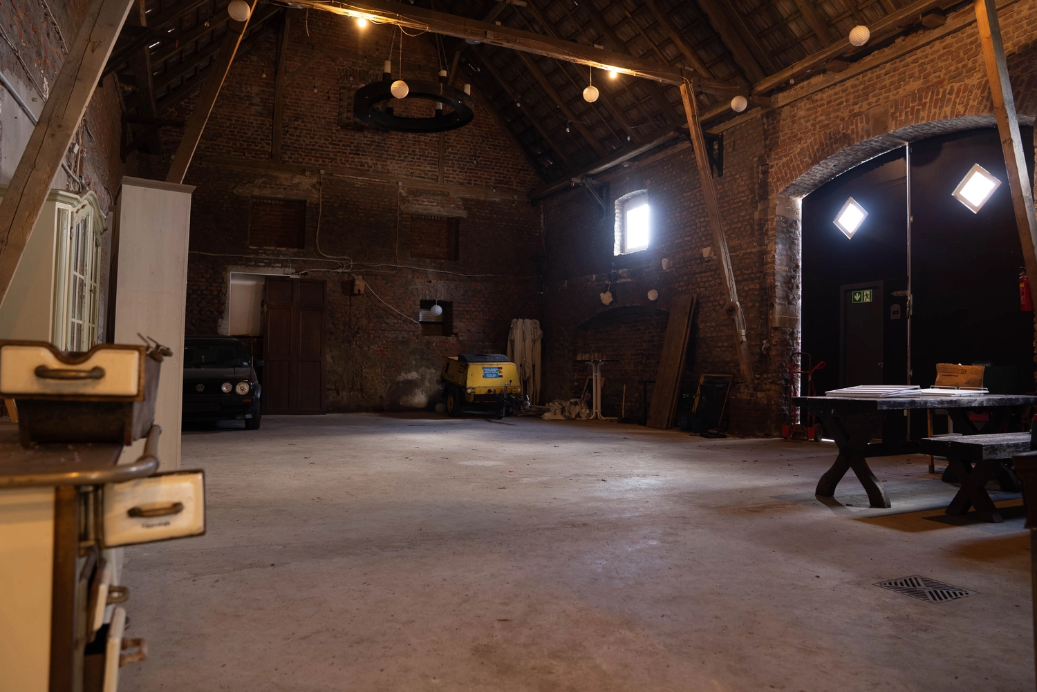 Alpakahof Dingen – Alpaka-Trekking – Das Bild zeigt eine ländliche Bauernhofszene mit Alpakas in einem hölzernen Unterstand und Gehege.