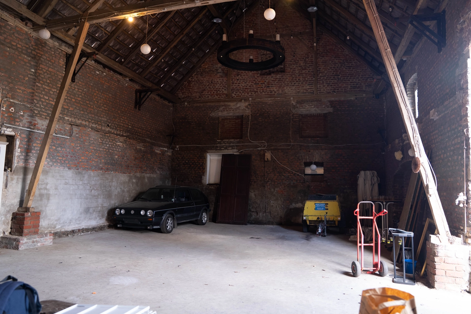 Alpakahof Dingen – Alpaka-Trekking – Das Bild zeigt eine ländliche Bauernhofszene mit Alpakas in einem hölzernen Unterstand und Gehege.