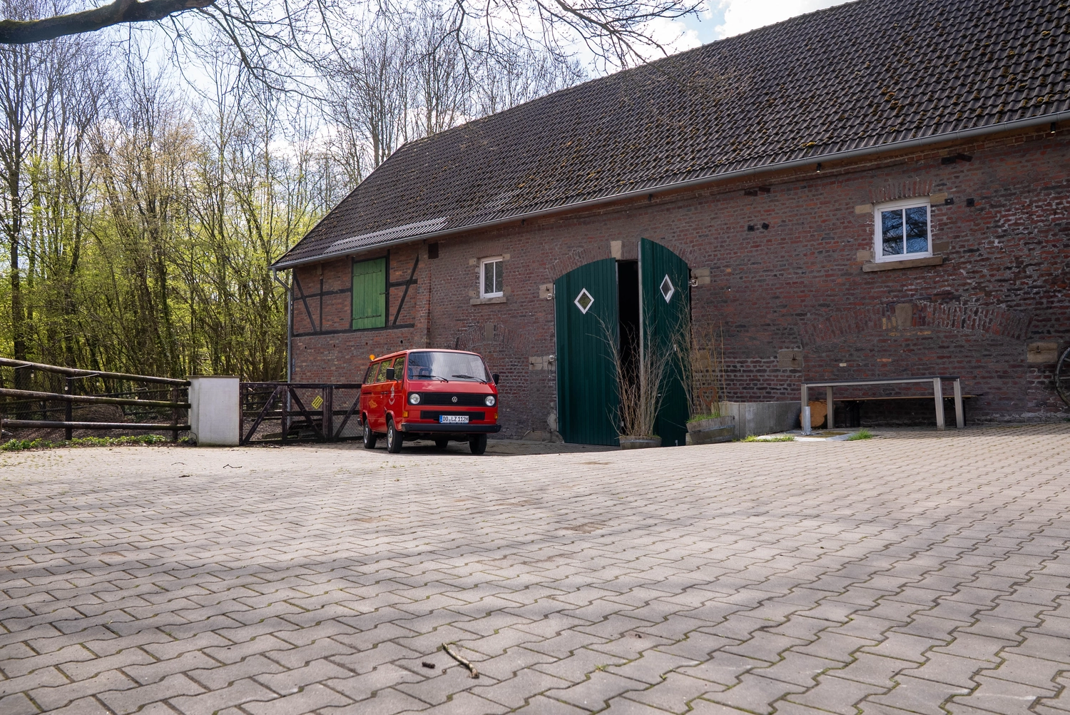 Alpakahof Dingen – Alpaka-Trekking – Das Bild zeigt eine ländliche Bauernhofszene mit Alpakas in einem hölzernen Unterstand und Gehege.