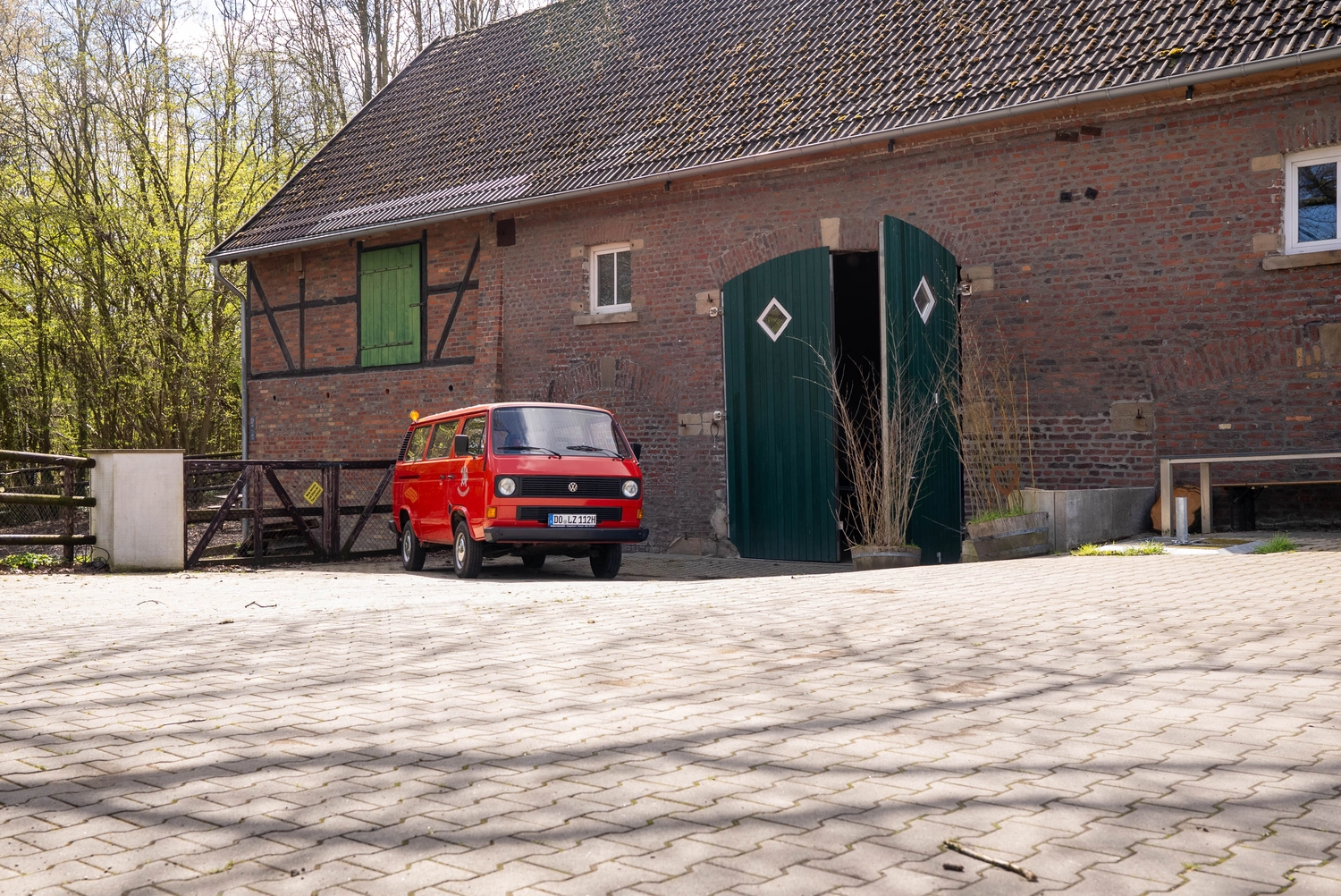 Alpakahof Dingen – Alpaka-Trekking – Das Bild zeigt eine ländliche Bauernhofszene mit Alpakas in einem hölzernen Unterstand und Gehege.